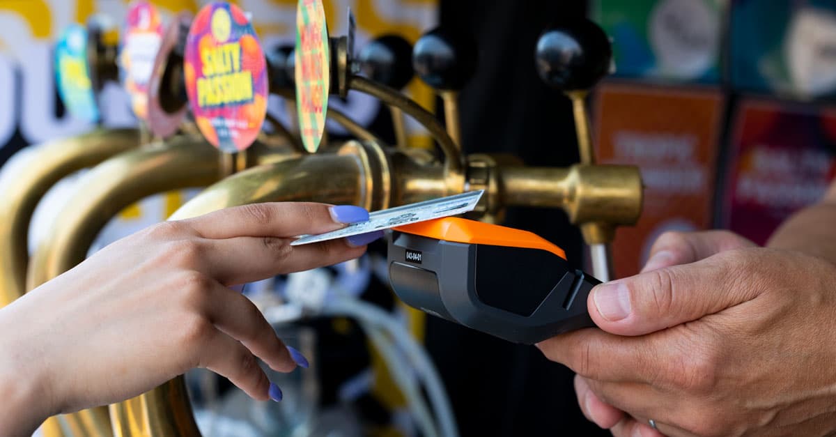 A customer pays by card on a handheld terminal in front of the beer taps.