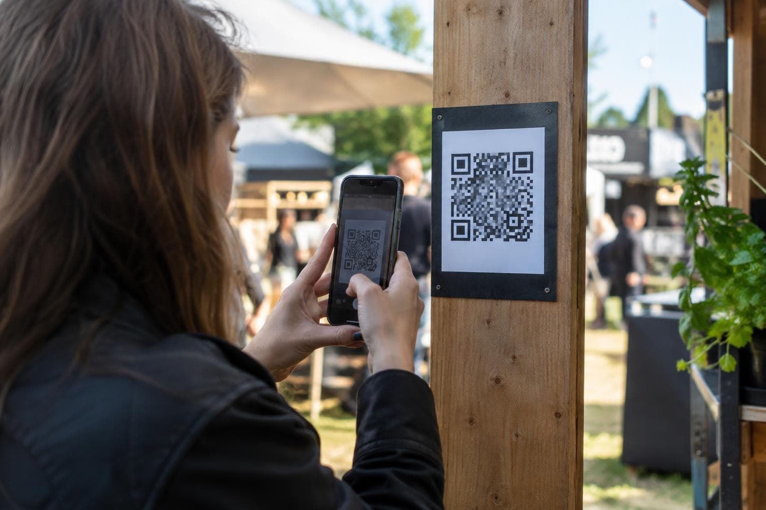 Henkilö suuntaa puhelintaan puupylvääseen kiinnitettyä QR-koodia kohti ulkotilassa.